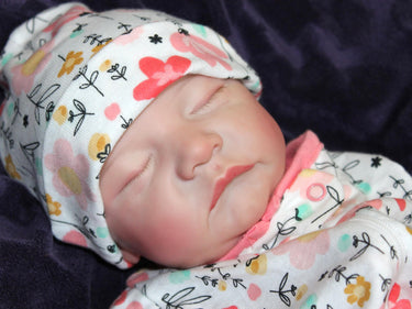A baby in pink floral pajamas peacefully lying down on a soft surface.